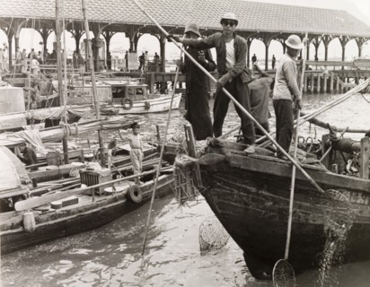 Fishing in a Hong Kong harbour. Fishermen stand at the bow of their sampan, dipping long-handled