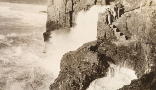 Watching the waves, Cornwall. A group of tourists stand on steps cut into a rocky outcrop on the