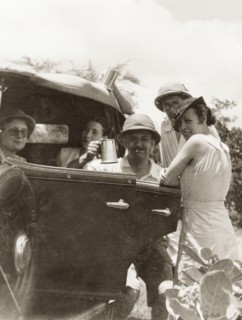 Friends socialising, Calcutta. A group of friends socialise by a motor car, one man raising up a