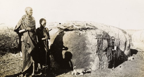 A traditional Maasai hut. A Maasai woman and two children stand beside a traditional Maasai wattle