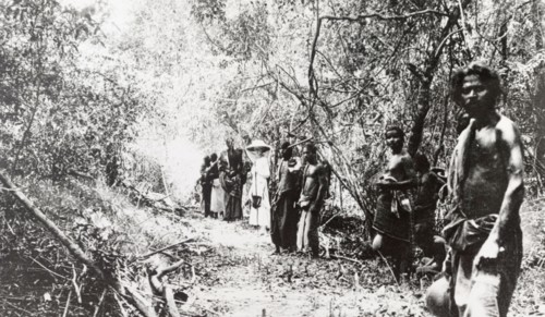 Beaters on an elephant drive, Ceylon. A European woman stands in a jungle clearing with a team of