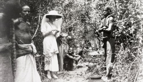 Ceylonian beaters on elephant drive. A European woman stands in a jungle clearing with a team of