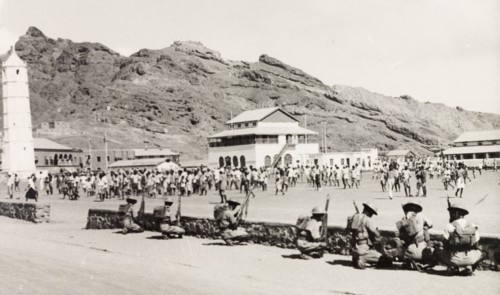 Policing the Aden riots, 1947. Armed police or soldiers form a defensive barrier behind a low wall,