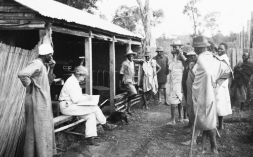 Pay day on a Kenyan farm. Kenyan farm hands gather around a European farmer's wife as she
