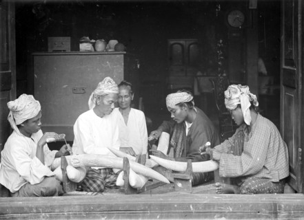 Carving elephant tusks, Burma. Four Burmese men sit on the floor of a workshop carving intricate