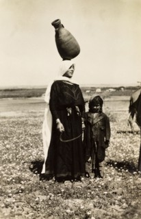 Bedouin woman carrying water pot. A bedouin woman stands with a young child in the Palestinian