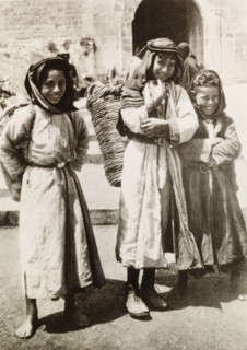 Child basket carriers, Palestine. Three Palestinian children pose on a city street, each carrying a