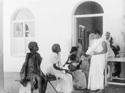 Queuing outside a mission hospital, India. Indian women and girls sit on a bench as they queue for