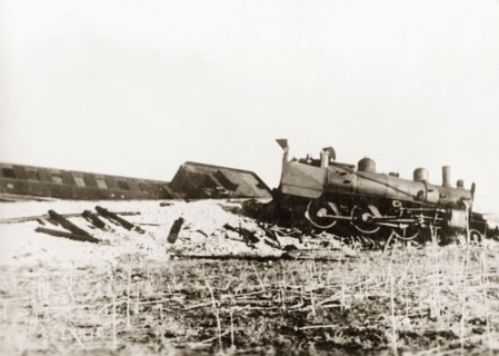 Derailed steam locomotive at Ras el Ain. A steam locomotive lies in pieces on a railway embankment,