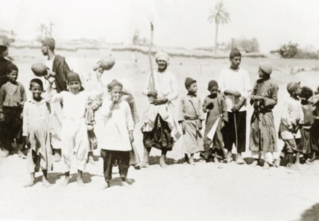 Palestinian villagers at harvest time. Men and boys stand in line with agricultural tools and