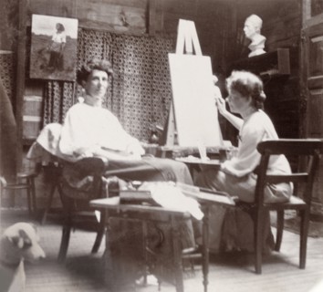 Minnie Murray poses for a painted portrait. Minnie Murray sits in a chair in an art studio, posing