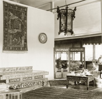 Asian artefacts in a colonial drawing room, British Malaya. Dr Reid Tweedie sits reading in the