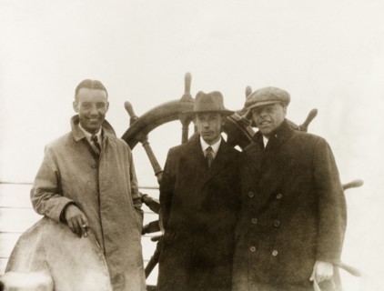 On voyage to India. Three British men on a sea voyage to India pose on deck beside the ship's wheel