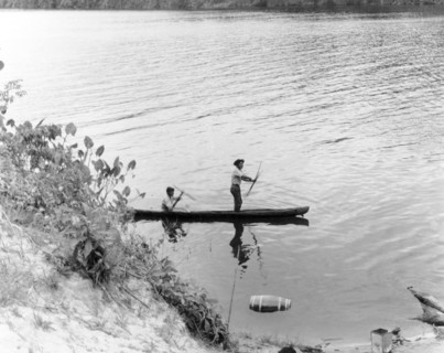 Traditional fishing in British Guiana. Two fishermen prepare their bows and arrows as they pilot a