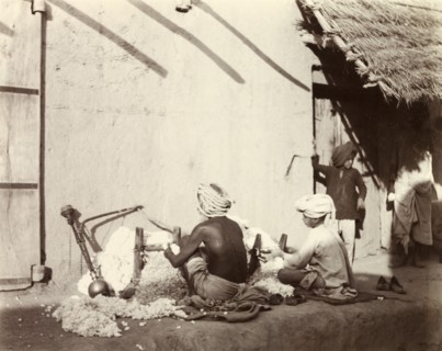 Indian cotton weavers. Two Indian men sit weaving cotton on the ground outside a mud-walled