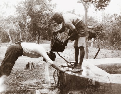 Showering at a well, Ceylon. A Ceylonian man pours a bucket of water from a well over a European