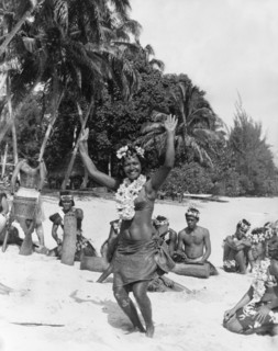 Performers on Moorea Island. A woman holds her hands in the air as she dances on a beach, dressed