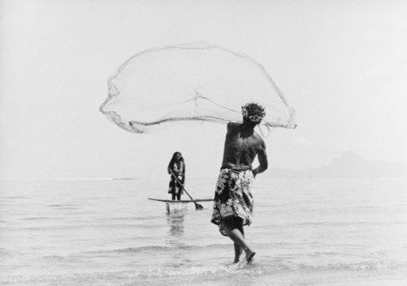Fishing with a cast net. A Tahitian man wearing a printed 'pareu' (sarong) hurls a cast net into