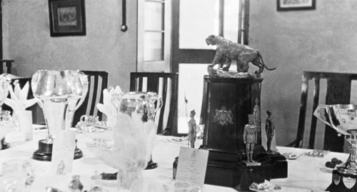A table set for a formal dinner. Various trophies form the centrepiece of a table that has been set