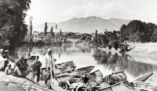 Evening on the Jhelum'. A group of men and small children mill about on a steep riverbank above the