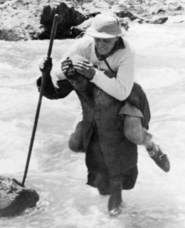 Crossing a Kashmiri Stream'. A Kashmiri trek porter carries a George Boon on his back as he