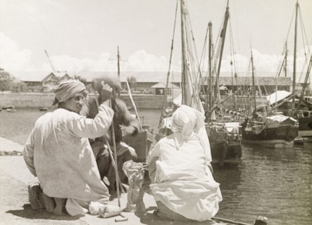 The Old Harbour at Stone Town. Three men sit beside the Old Harbour at Stone Town, with several