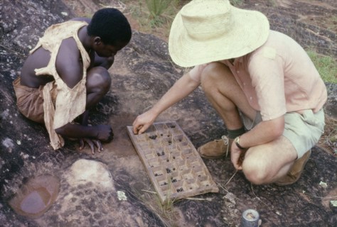 Playing omweso at Kojja. A British man identified as Martin Beadle squats down to play omweso
