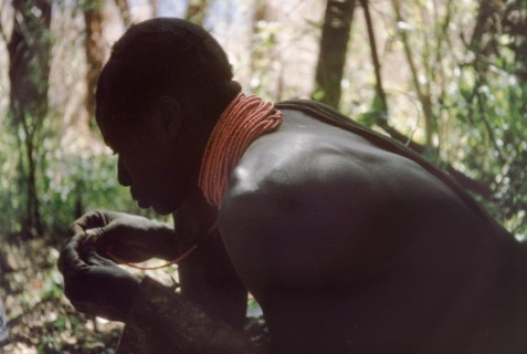 Rescuing a broken necklace. A Karamojong porter working with a British forestry survey team rescues