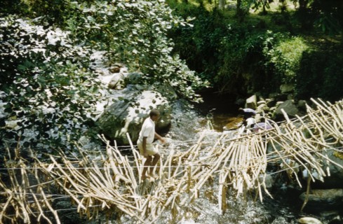 Ramshackle rope bridge in Kyarumba. A man crosses an old, ramshackle rope bridge above a river in