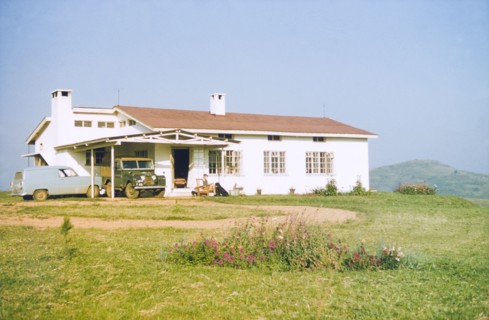 Bungalow in Fort Portal. District Forestry Officer James Lang Brown sits reading in an armchair
