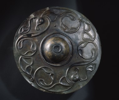 Decorated in a combination of repousse and incision style with two large birds whose wings develop into tendril motifs, this bronze boss is all that remains of a Celtic shield which was found in the T...