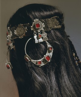 A silver headband from which hang large circular earrings inlaid with glass