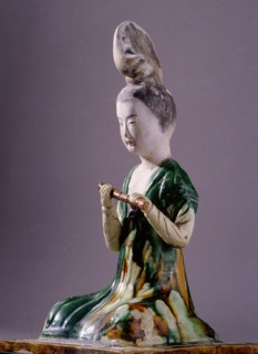 Figure of a kneeling female musician with a distinctive high chignon hairstyle, holding a flute