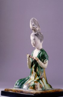 Figure of a kneeling female musician with a distinctive high chignon hairstyle, holding a flute