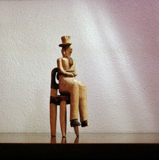 A carving of a white man wearing a top hat seated on a European style chair