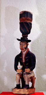 Drum with support carved as the figure of a seated European trader with gin bottle and glass