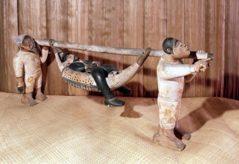 A carving of a European carried in a hammock