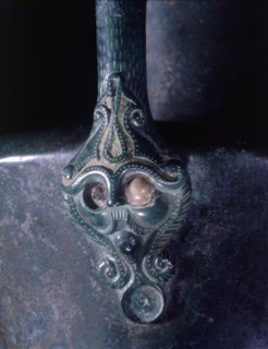 Lower handle attachment of a bronze jug represents a bearded and moustached head which is crowned with an emblematic representation of the Tree of Life