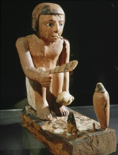 A male cook fans the fire in preparation for roasting the duck he holds in his left hand