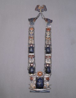 A scarab pectoral from the tomb of Tutankhamun with straps formed from inlaid plaques with uraei (cobras), scarabs & solar discs