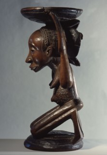 Chiefs stool supported by kneeling woman