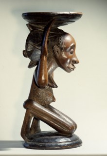 Chiefs stool supported by kneeling woman