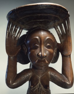 Chiefs stool supported by kneeling woman