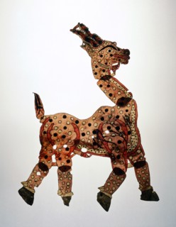 A shadow puppet in the form of a yellow prancing horse, decorated with black and white spots