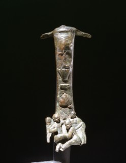 Bronze handle from an oinochoe, decorated in relief with scene of two dwarves boxing or wrestling, watched by an umpire