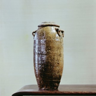 A tall thin vase with a lid, coated with a black glaze