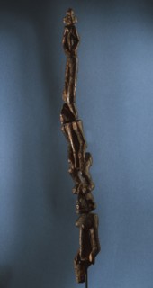 A wood sculpture of three figures standing one on top of the other