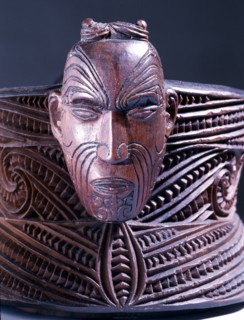A oval lidded wooden box with scrolled carvings on the sides and a male and female head carved at the ends