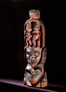 Model totem pole with paired figures below bird crest