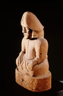 Seated wooden figure with large earrings and a phallus shaped headdress
